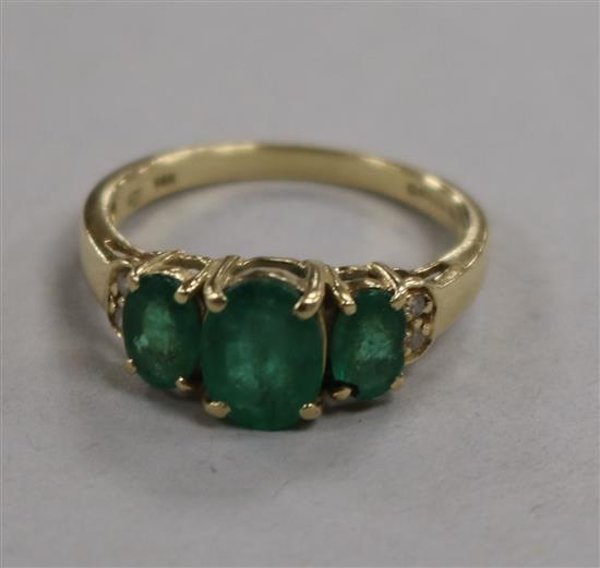 A 14ct gold, three stone emerald ring with diamond chip shoulders, size P.